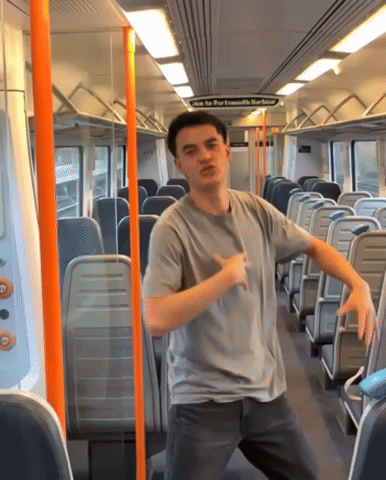 a man in a grey shirt is dancing on a train with a sign above him that says " come to port ismouth barbour "