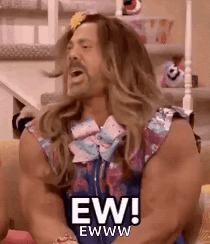 A long-haired muscular man in a colorful outfit exclaims “EW!” indoors.