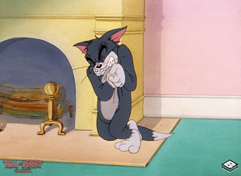 Tom from Tom and Jerry covers his face while standing by a small table.