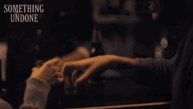a bottle of something undone sits on a table next to a couple 's hands