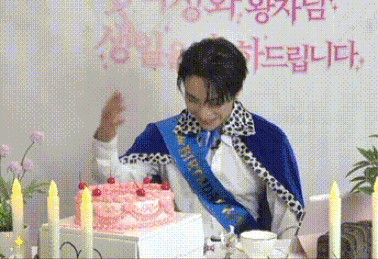 a man in a blue cape is standing in front of a birthday cake with cherries on it .