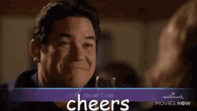 a man with a glass of wine in front of a sign that says cheers