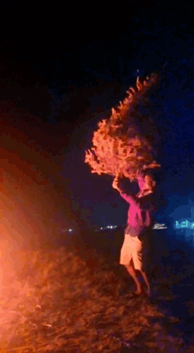 a person is standing in front of a fire holding a christmas tree