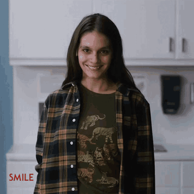 A woman in a plaid overshirt stands smiling directly at the camera.