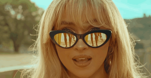 a close up of a woman wearing sunglasses with a beach scene reflected in them