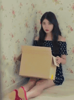 A woman holds a cardboard box in front of a floral wall.