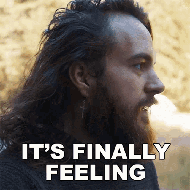 a man with long hair and a beard has the words it 's finally feeling above his head