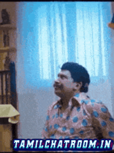 a man in a polka dot shirt is standing in front of a window with tamilchatroom.in written on the bottom right
