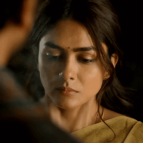 A woman looks downward with a serious, tearful expression.