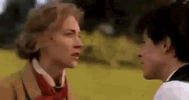 two women are standing next to each other in a field and looking at each other .