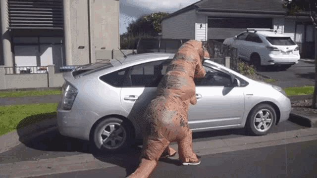 a person dressed as a t-rex is standing next to a silver prius