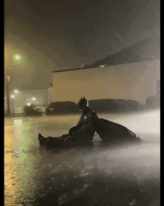 A lone dark figure sits on a snowy street at night under streetlights.