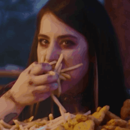 A woman eats a handful of fries in a dim restaurant scene.