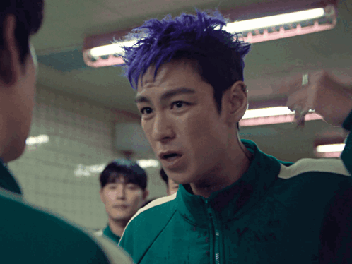 a man with purple hair in a green jacket talks to another man