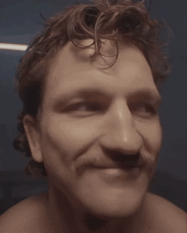 A shirtless man raises one eyebrow with a subtle smirk.