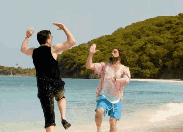 Two people jump toward each other on a sunny beach.