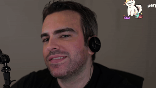 a man wearing headphones looks at the camera in front of a sticker of a white cat with a crown on its head