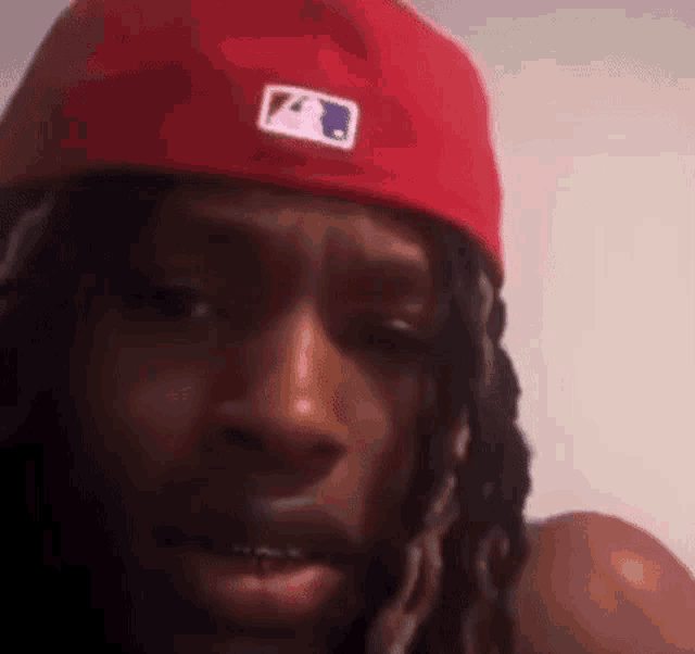 a man wearing a red hat and dreadlocks is looking at the camera .