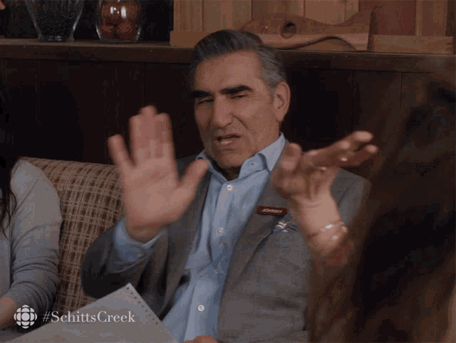 Johnny Rose holds both hands up in a wary, hesitant gesture.