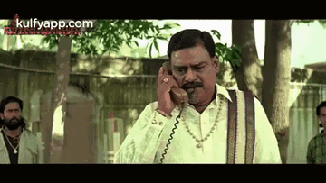 a man is talking on a cell phone while standing in front of trees .