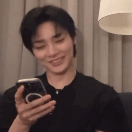 a man is sitting on a couch holding a cell phone in his hand and smiling .