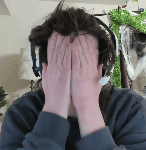 A headset-wearing person covers their face with both hands at a desk.