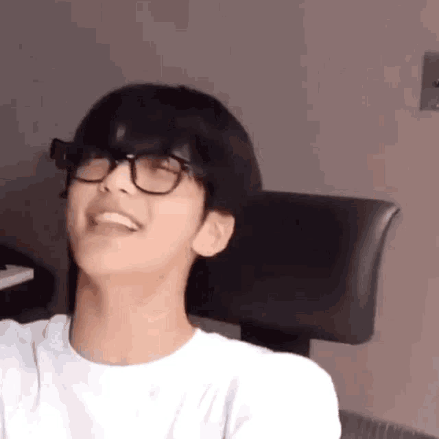 a young man wearing glasses and a white shirt is smiling while sitting in a chair .