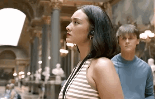 a woman wearing headphones stands next to a man in a blue shirt in a museum .