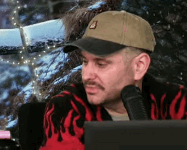 a man wearing a hat and a sweater is sitting in front of a laptop computer .