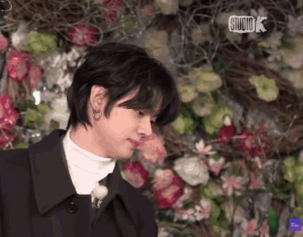 a close up of a person in front of a wall of flowers with studio k written on the bottom