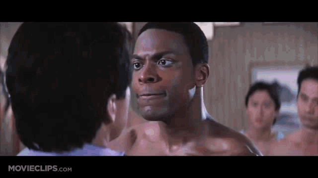 a man without a shirt is talking to another man in a room .