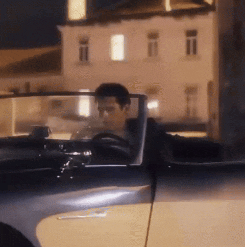 a man is driving a convertible car at night in front of a building