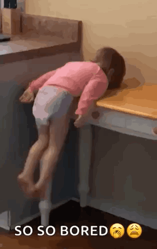 A child sprawls across a kitchen counter beneath “SO SO BORED.”