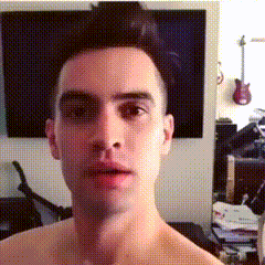 a man without a shirt is looking at the camera with a guitar hanging on the wall behind him