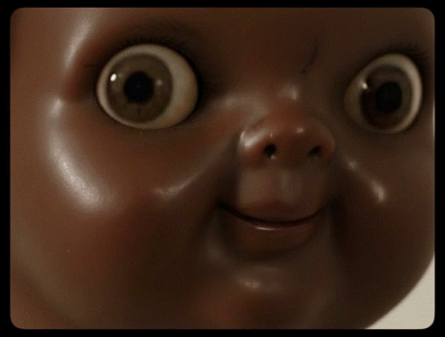 A glossy doll-like face stares ahead with enormous unblinking eyes.