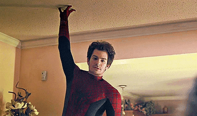 a man in a spiderman costume is reaching up to the ceiling .