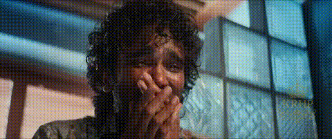 a man with curly hair is covering his mouth with his hands in a room .