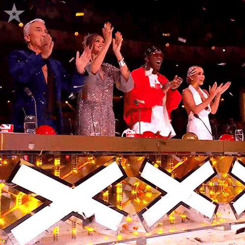 a group of people applauding in front of a sign that has the letter x on it