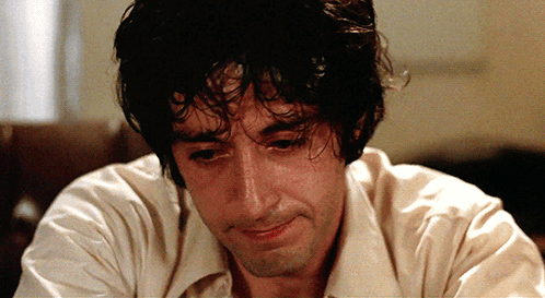 a man with curly hair and a white shirt looks down