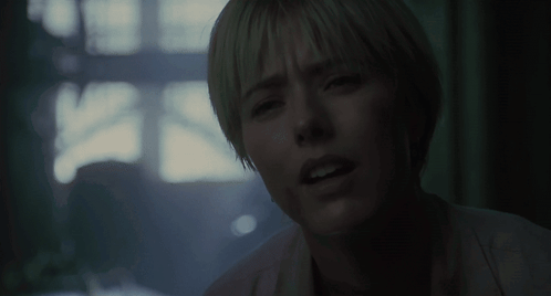 A woman in a dim scene looks over with a puzzled, distracted expression.