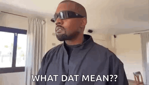 a man wearing sunglasses and a black jacket is standing in a living room and asking what dat mean .