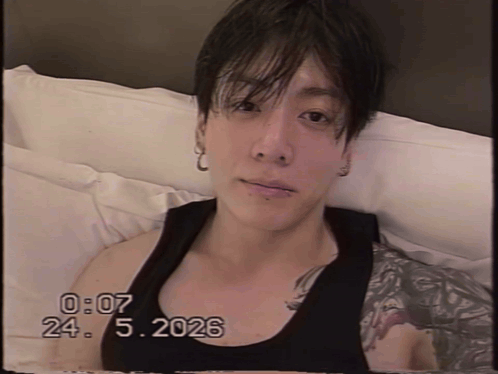 A man lounges on a couch in a black tank top with a timestamp overlay.