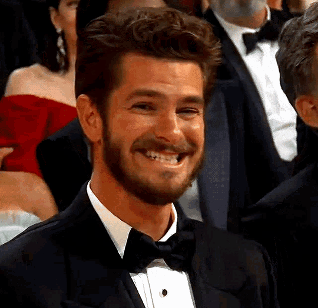 Andrew Garfield smiles tensely while seated at an awards event.