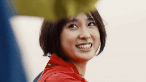 a close up of a woman 's face with short hair and a red jacket smiling .