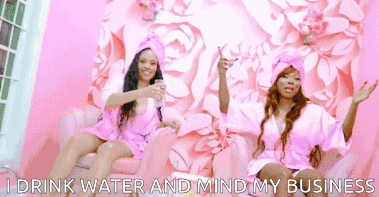 two women in pink robes are sitting on a pink couch drinking water