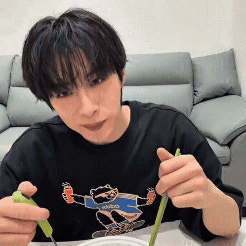 a man wearing a black shirt with a raccoon on it is eating with chopsticks