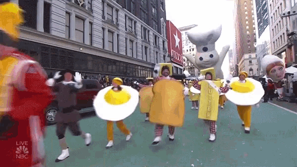 a group of people dressed in food costumes are walking down a street in front of a building that says nbc