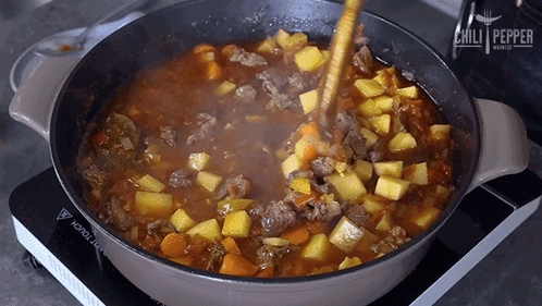 a pot of stew is being stirred with a wooden spoon by chili pepper
