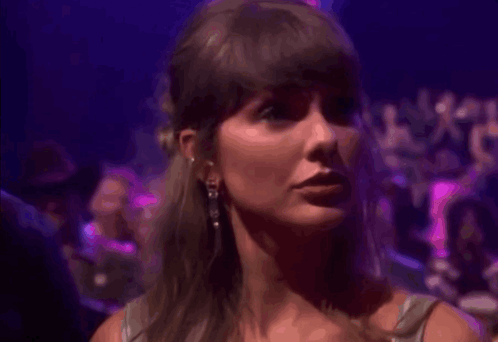 Taylor Swift glances sideways under purple concert lighting.