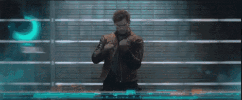 a man in a leather jacket is standing in front of a brick wall in a dark room .